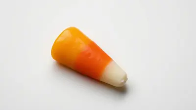 A single candy corn candy with orange, yellow, and white stripes on a white background.