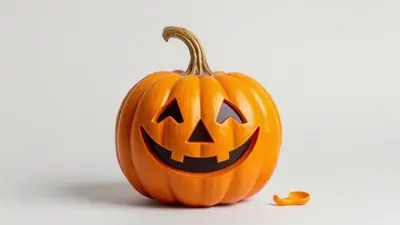 A carved jack-o-lantern with a smiling face sits on a white surface, with its stem curving upwards and a small piece of carved pumpkin to its right.