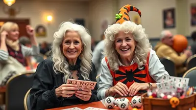 Two smiling elderly women are playing bingo at a Halloween-themed event. The woman on the right wears a festive witch hat and a spiderweb-themed vest, while the woman on the left holds a bingo card. Bingo balls and candy are visible on the table in front of them.