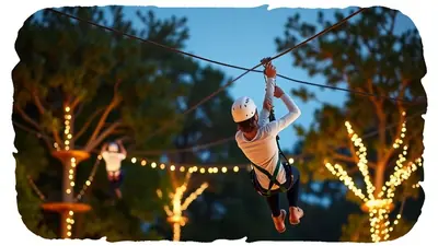 A person wearing a white helmet and harness is zip-lining through trees decorated with warm string lights at dusk.