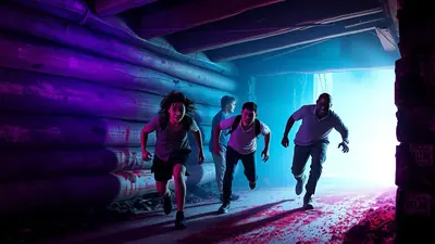 Four people are running away from something in a dimly lit, spooky wooden structure. The scene is illuminated by purple and blue lights, and the floor is covered in red debris.
